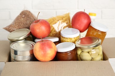 Photo of Different food products for donation in box near white brick wall, closeup