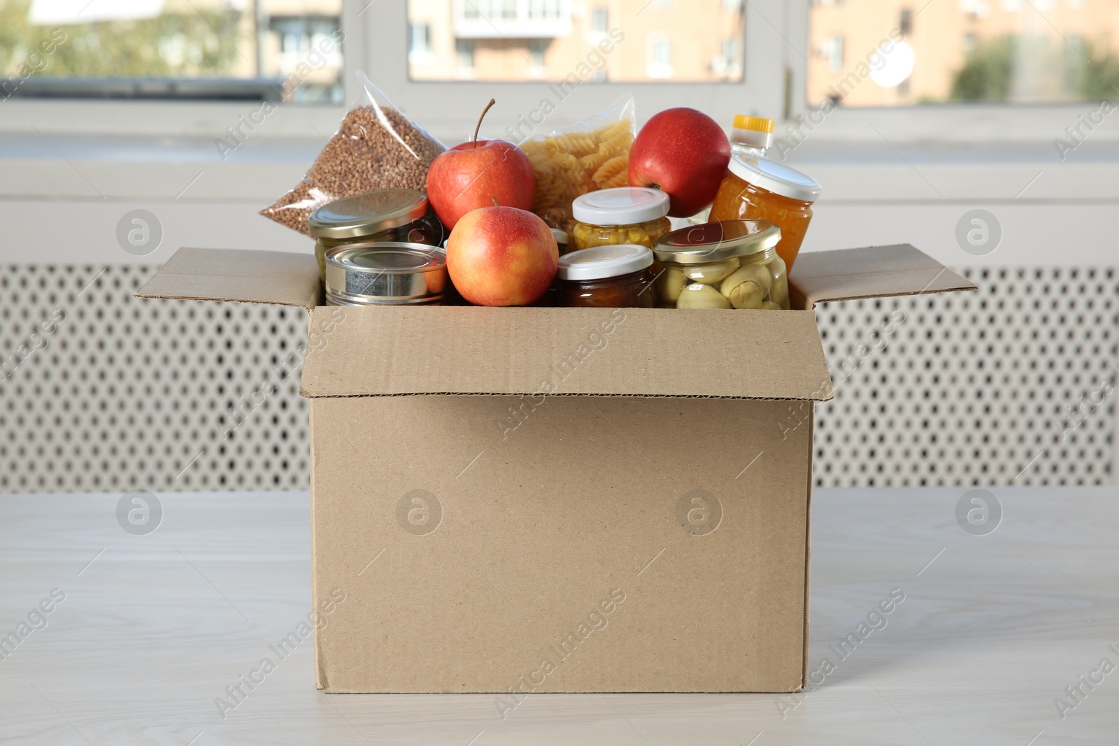 Photo of Different food products for donation in box on wooden table indoors