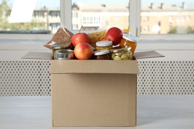 Photo of Different food products for donation in box on wooden table indoors