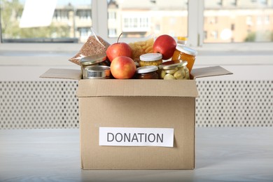 Photo of Different food products for donation in box on wooden table indoors