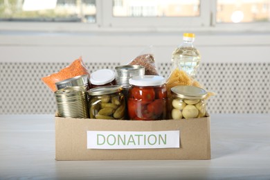 Photo of Different food products for donation in box on wooden table indoors