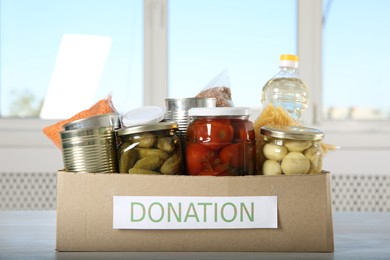 Photo of Different food products for donation in box on wooden table indoors