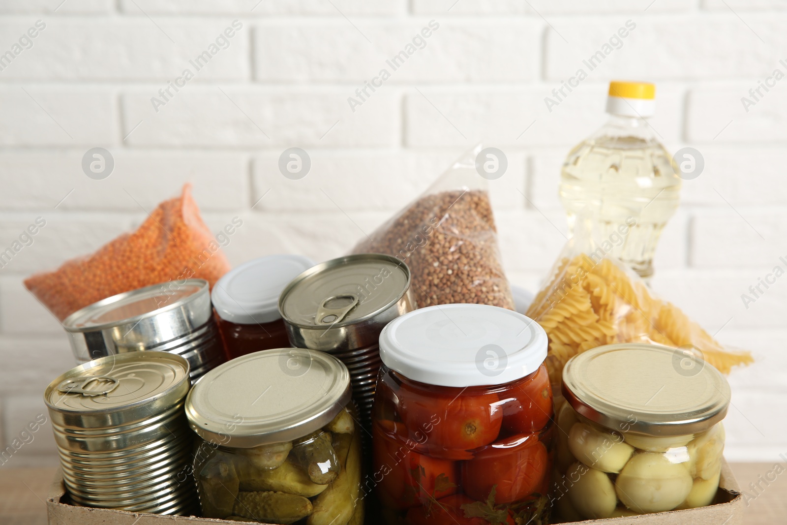 Photo of Different food products for donation in box on near white brick wall, closeup