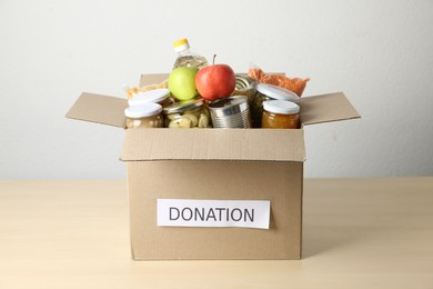 Photo of Different food products for donation in box on wooden table indoors