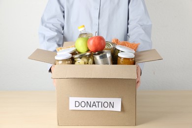 Photo of Food donation. Woman with box of different products at wooden table indoors, closeup