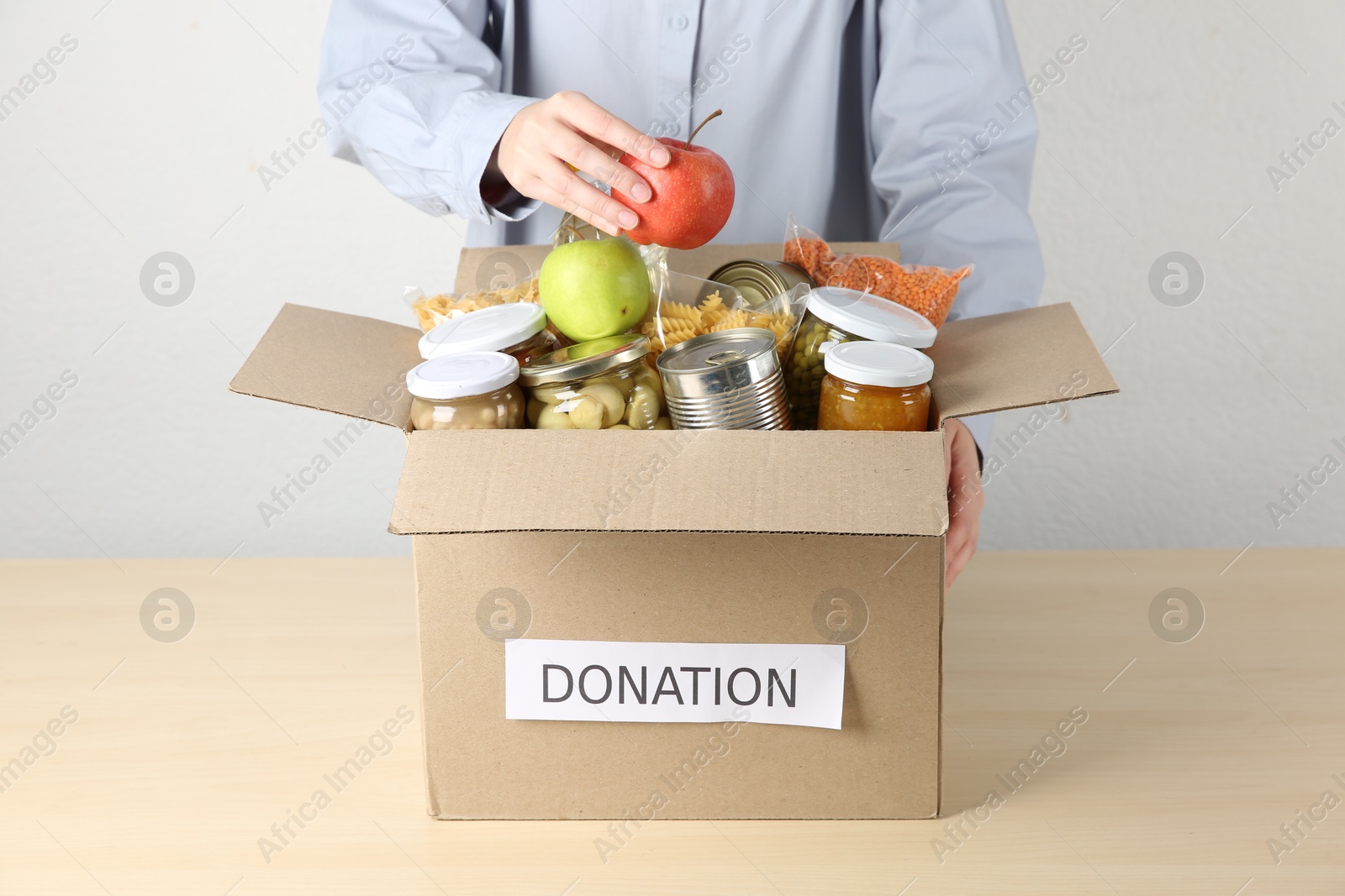 Photo of Woman packing different food products for donation at wooden table indoors, closeup