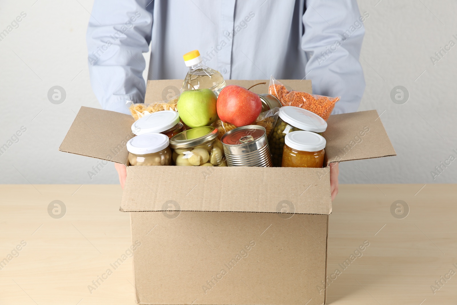 Photo of Food donation. Woman with box of different products at wooden table indoors, closeup