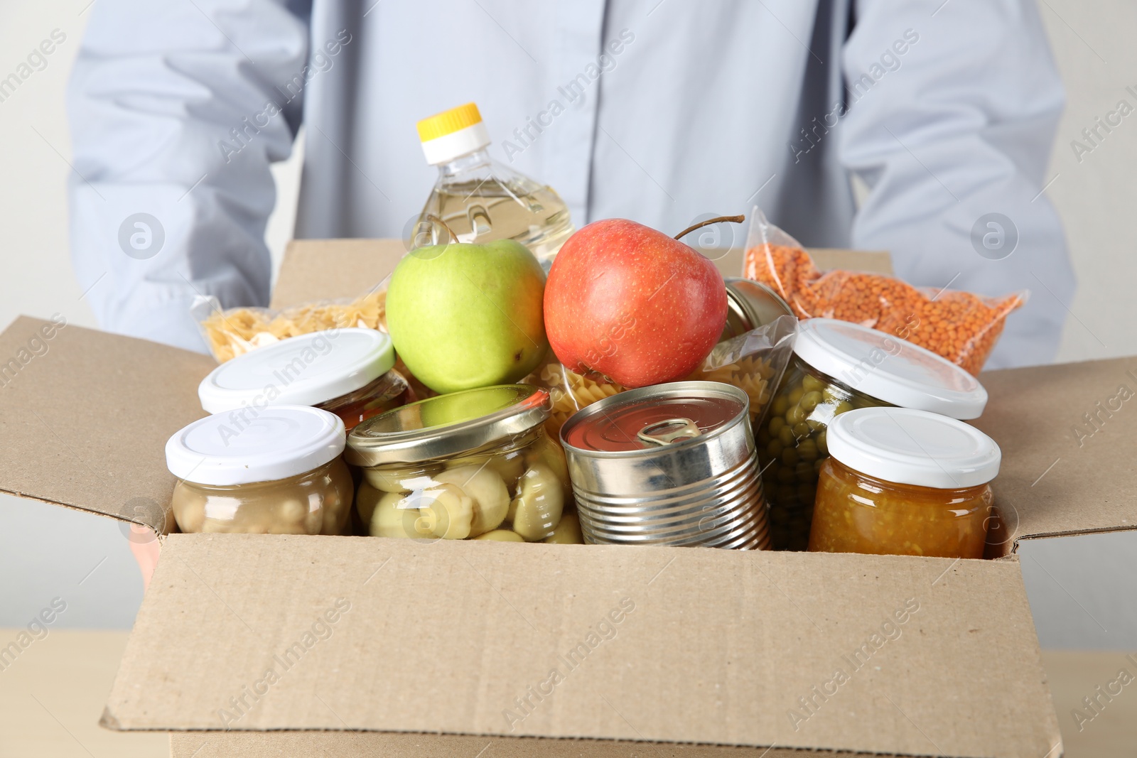 Photo of Food donation. Woman with box of different products at table indoors, closeup