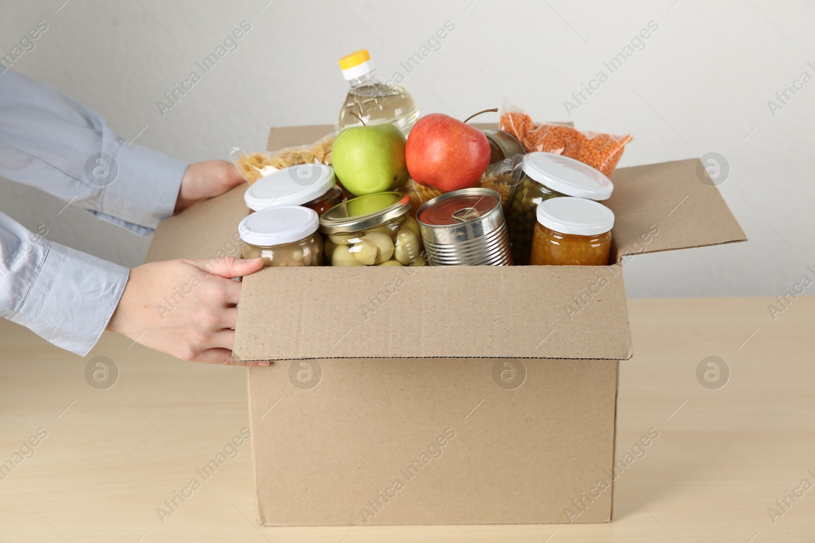 Photo of Food donation. Woman with box of different products at wooden table indoors, closeup