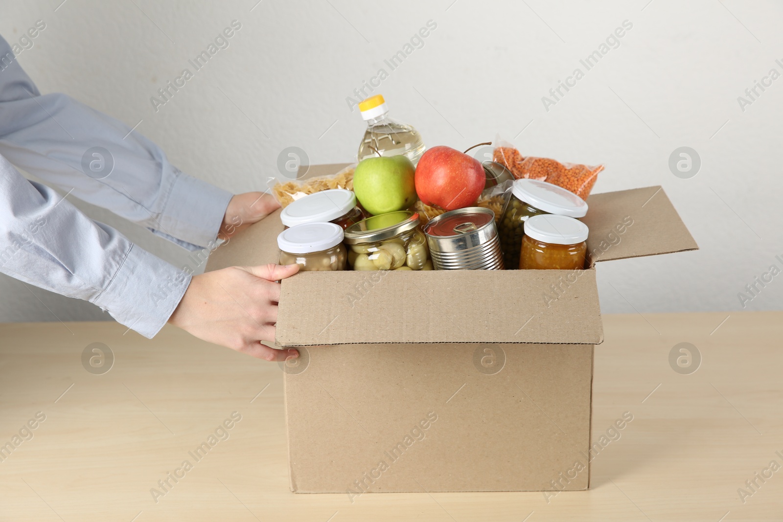 Photo of Food donation. Woman with box of different products at wooden table indoors, closeup