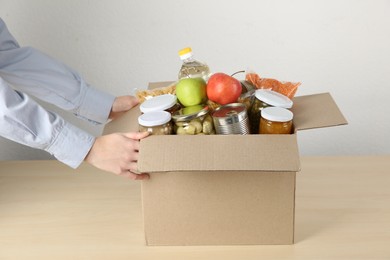 Photo of Food donation. Woman with box of different products at wooden table indoors, closeup