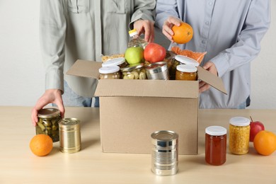 Photo of Women packing different food products for donation at wooden table indoors, closeup