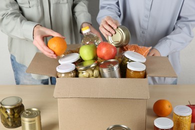 Photo of Women packing different food products for donation at wooden table indoors, closeup