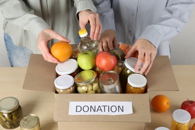 Photo of Women packing different food products for donation at wooden table indoors, closeup