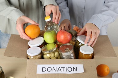 Photo of Women packing different food products for donation at table indoors, closeup