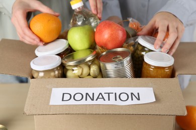 Photo of Women packing different food products for donation at table indoors, closeup