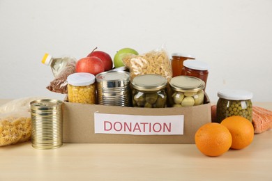 Photo of Different food products for donation in box on wooden table indoors