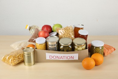 Photo of Different food products for donation in box on wooden table indoors