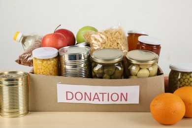 Photo of Different food products for donation in box on wooden table indoors, closeup