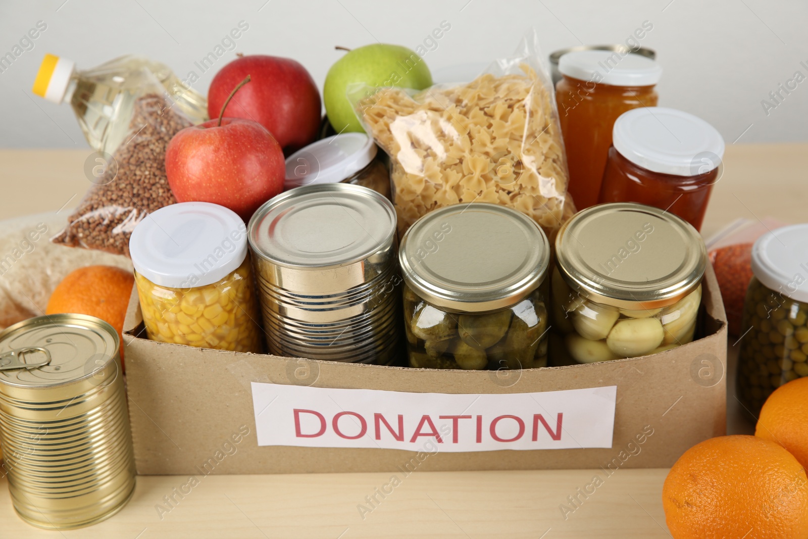 Photo of Different food products for donation in box on wooden table indoors, closeup