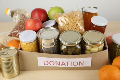 Photo of Different food products for donation in box on wooden table indoors, closeup