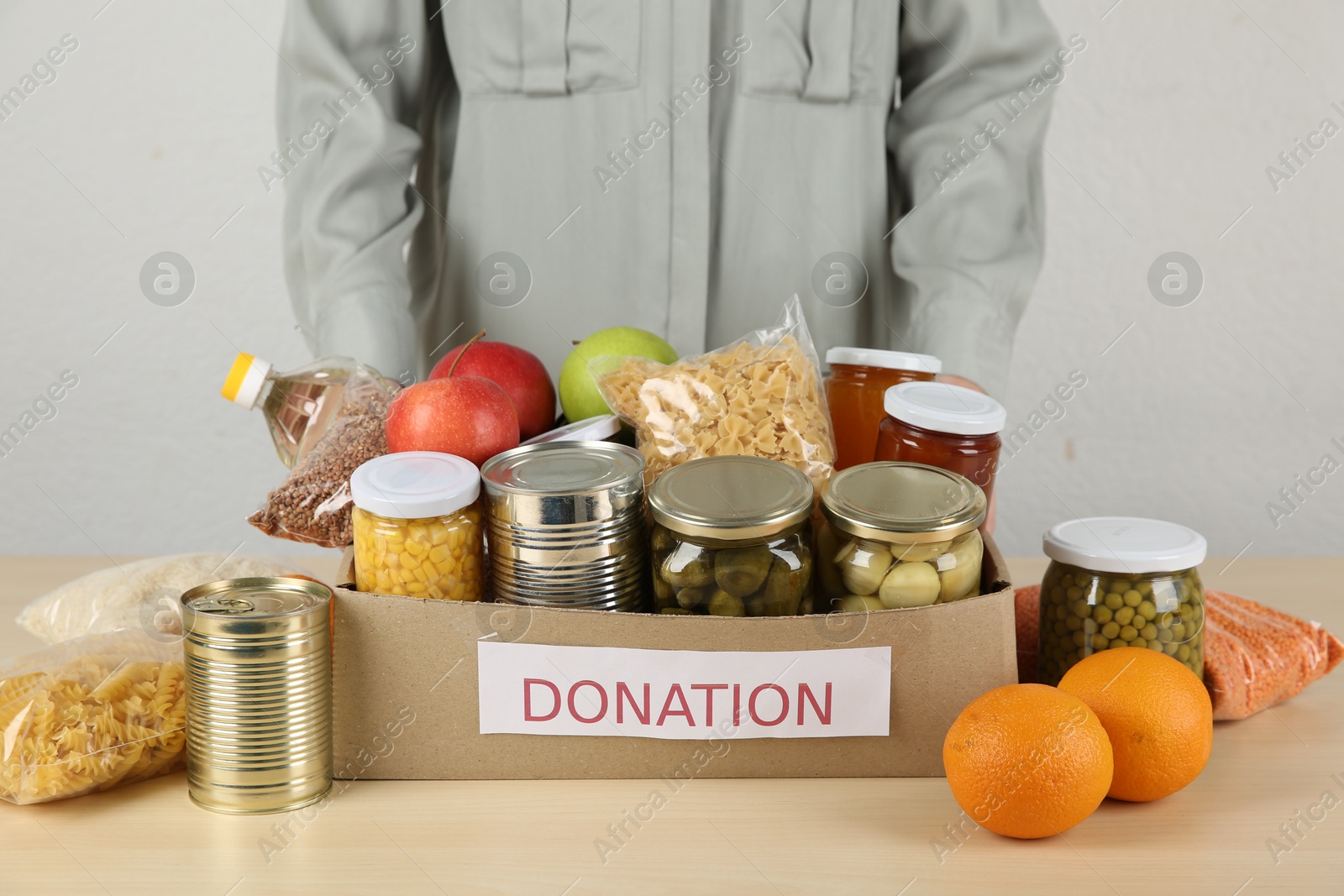 Photo of Food donation. Woman with box of different products at wooden table indoors, closeup