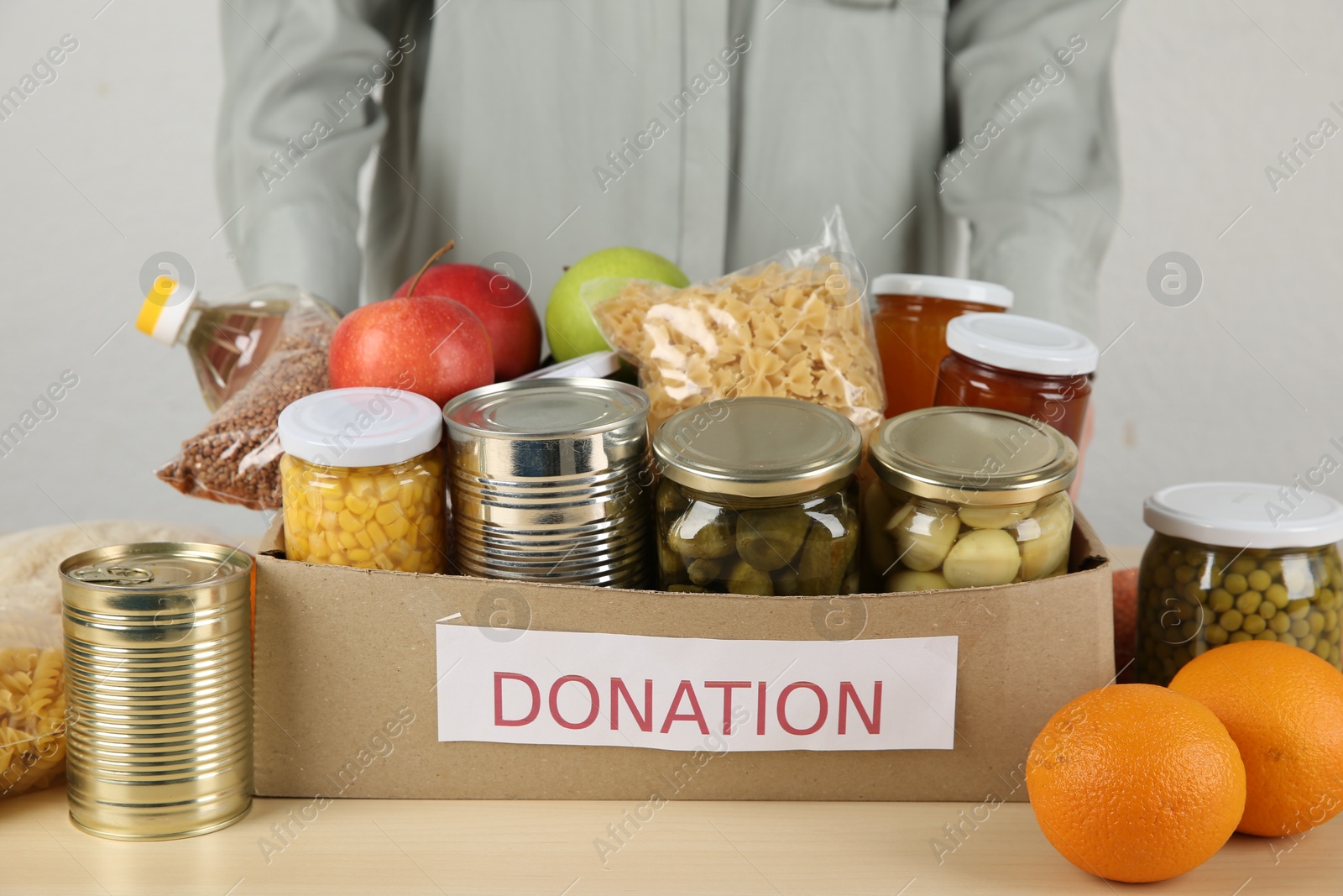 Photo of Food donation. Woman with box of different products at wooden table indoors, closeup