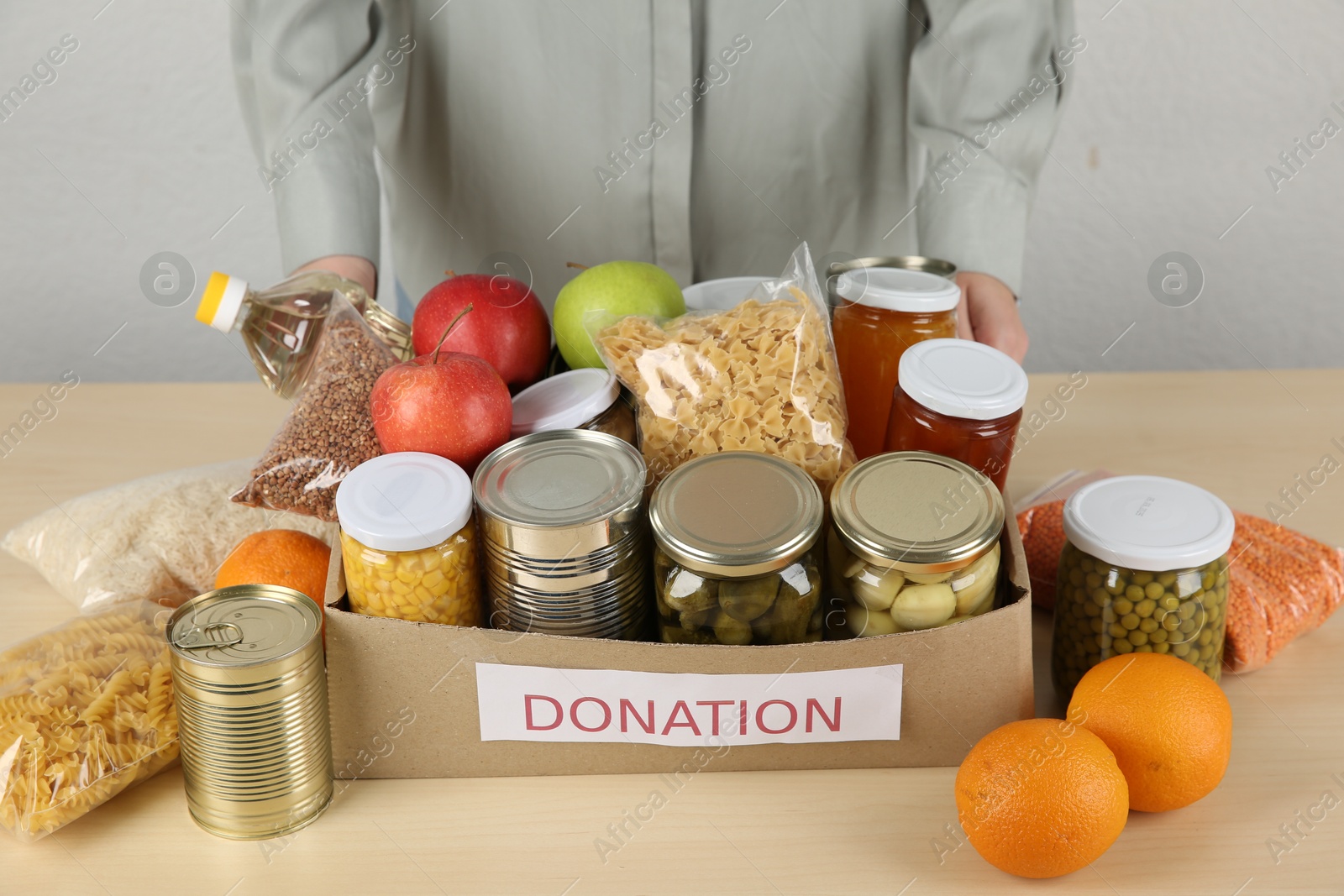 Photo of Food donation. Woman with box of different products at wooden table indoors, closeup