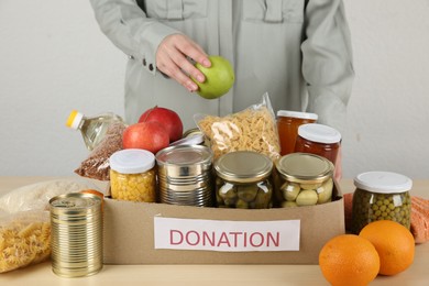 Photo of Woman packing different food products for donation at wooden table indoors, closeup