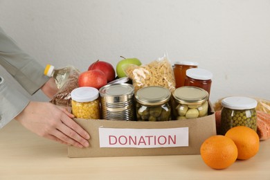 Photo of Food donation. Woman with box of different products at wooden table indoors, closeup