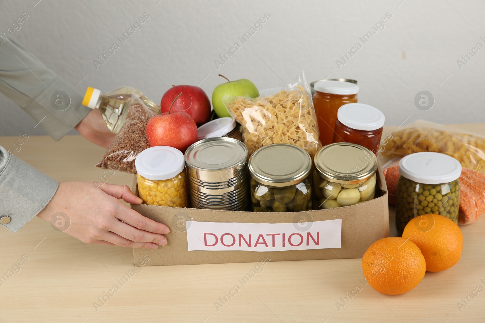 Photo of Food donation. Woman with box of different products at wooden table indoors, closeup