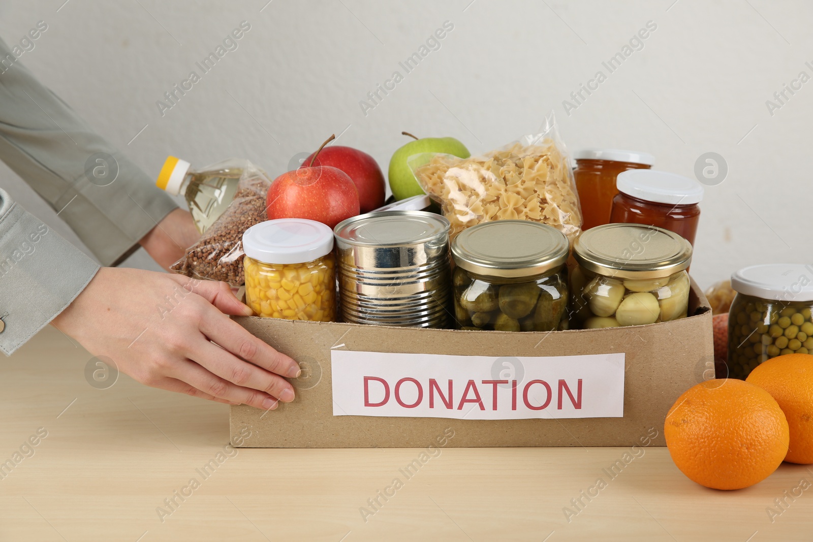 Photo of Food donation. Woman with box of different products at wooden table indoors, closeup