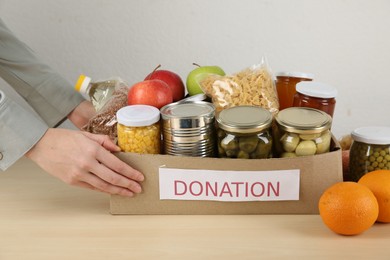 Photo of Food donation. Woman with box of different products at wooden table indoors, closeup