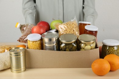 Photo of Food donation. Woman with box of different products at wooden table indoors, closeup