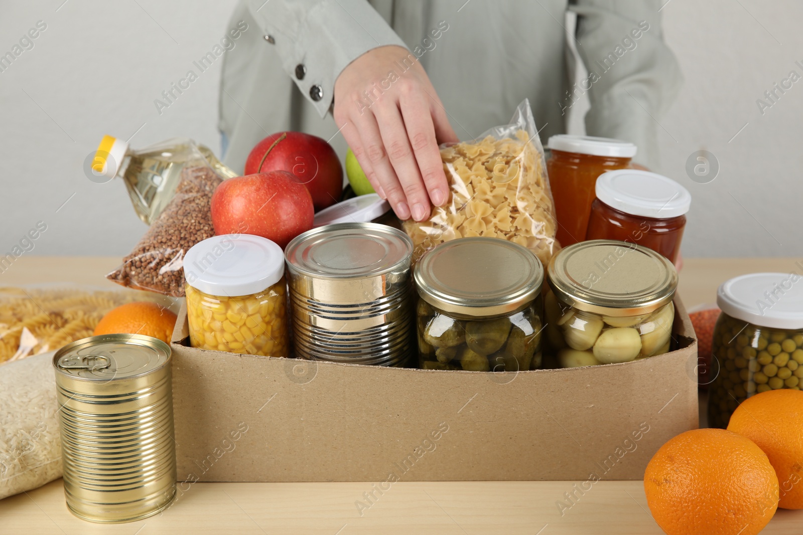 Photo of Woman packing different food products for donation at wooden table indoors, closeup