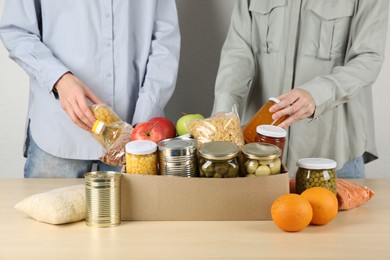 Photo of Women packing different food products for donation at wooden table indoors, closeup