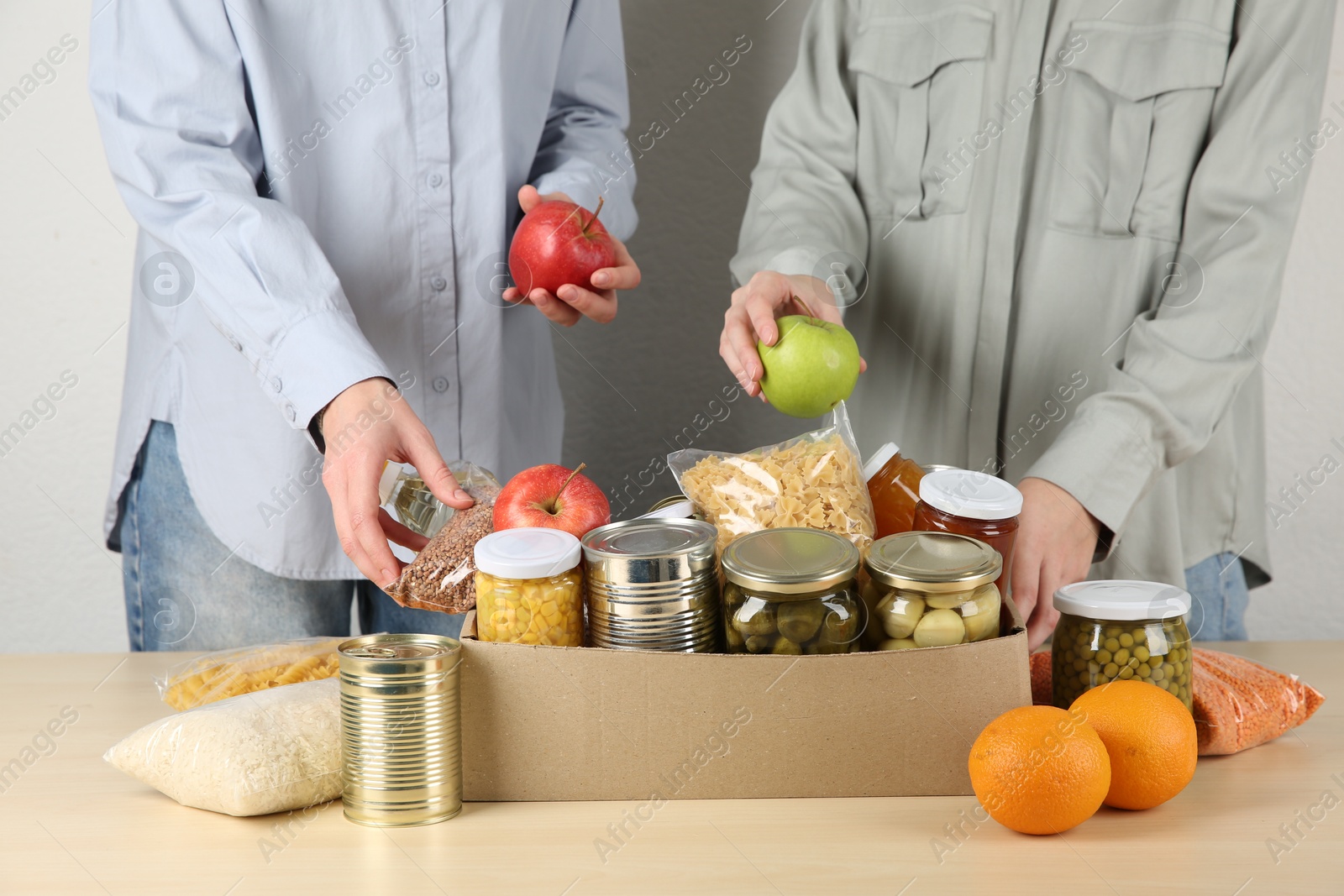 Photo of Women packing different food products for donation at wooden table indoors, closeup