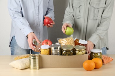 Photo of Women packing different food products for donation at wooden table indoors, closeup