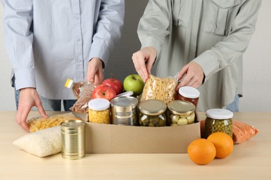 Photo of Women packing different food products for donation at wooden table indoors, closeup