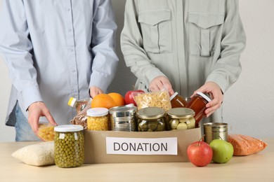 Photo of Women packing different food products for donation at wooden table indoors, closeup