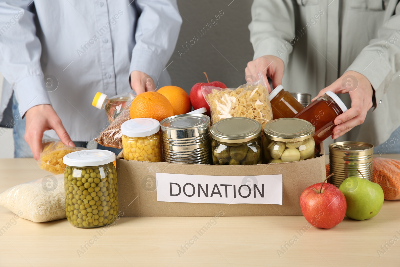 Photo of Women packing different food products for donation at wooden table indoors, closeup