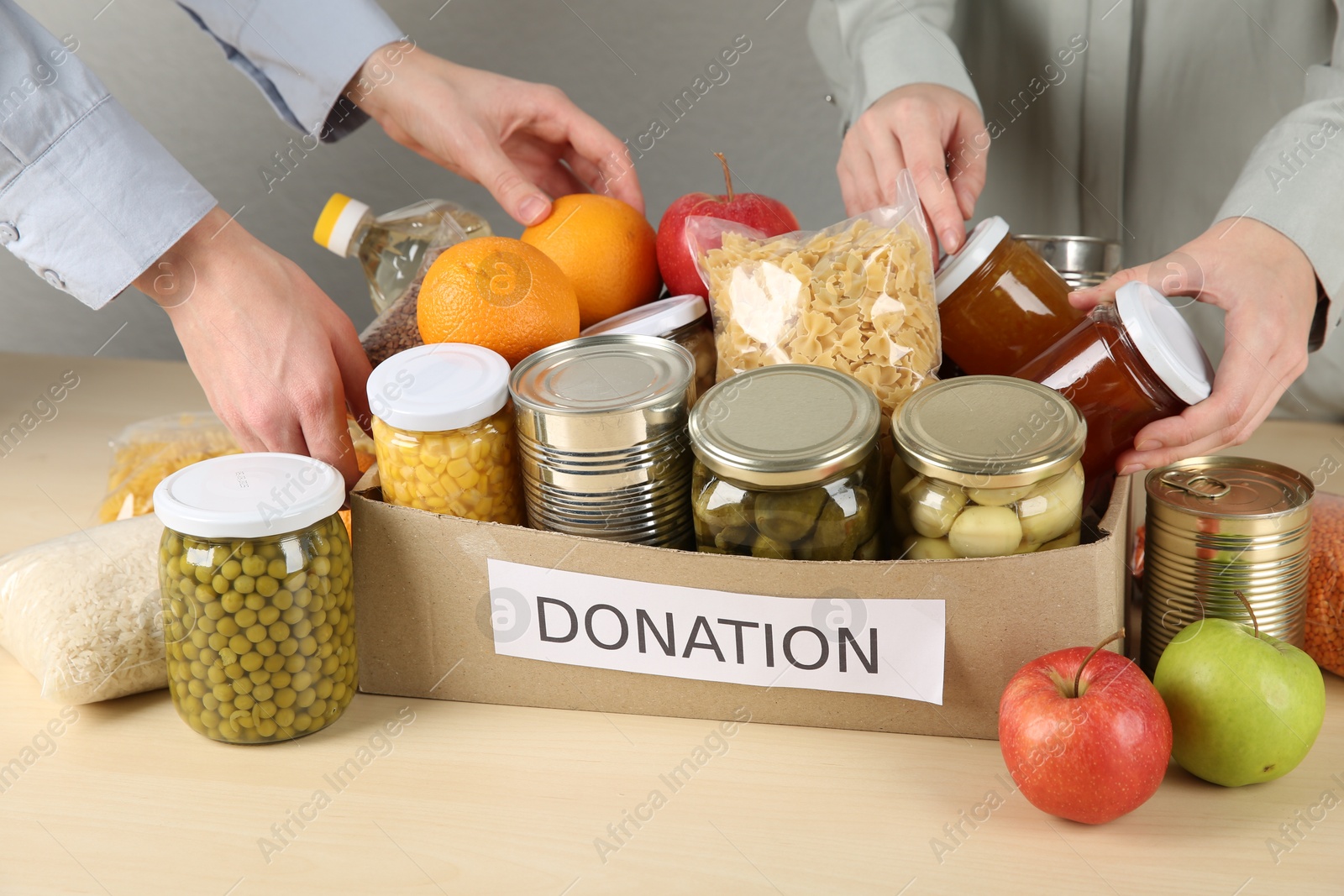 Photo of Women packing different food products for donation at wooden table indoors, closeup