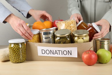 Photo of Women packing different food products for donation at wooden table indoors, closeup