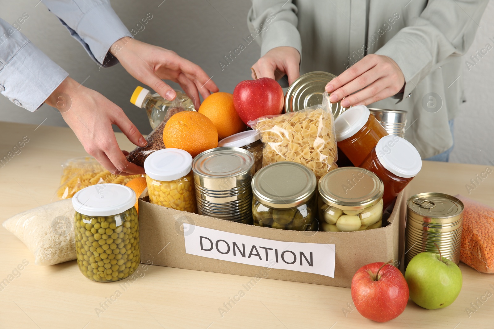 Photo of Women packing different food products for donation at wooden table indoors, closeup