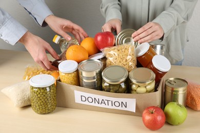 Photo of Women packing different food products for donation at wooden table indoors, closeup