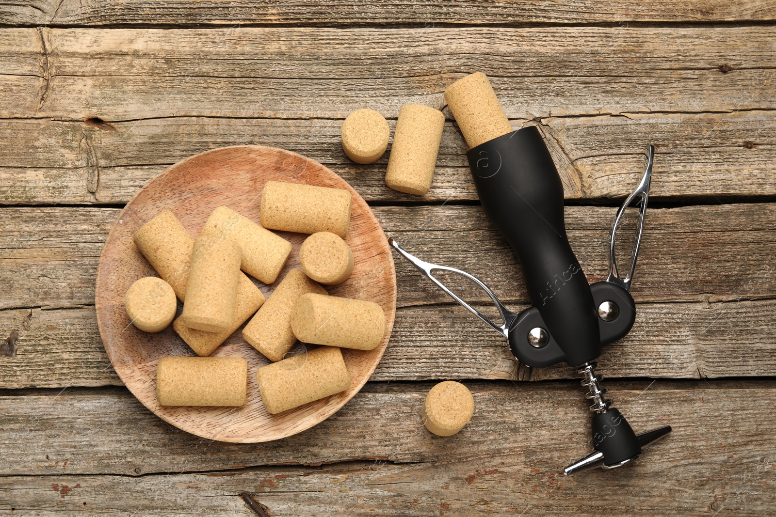 Photo of Wing corkscrew and corks on wooden table, flat lay