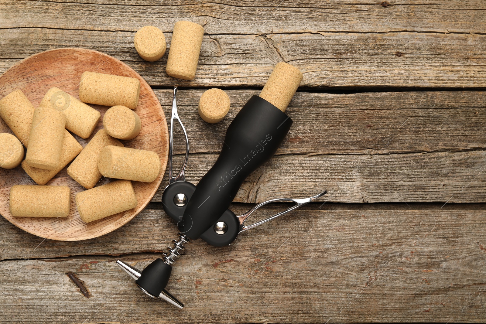 Photo of Wing corkscrew and corks on wooden table, flat lay. Space for text