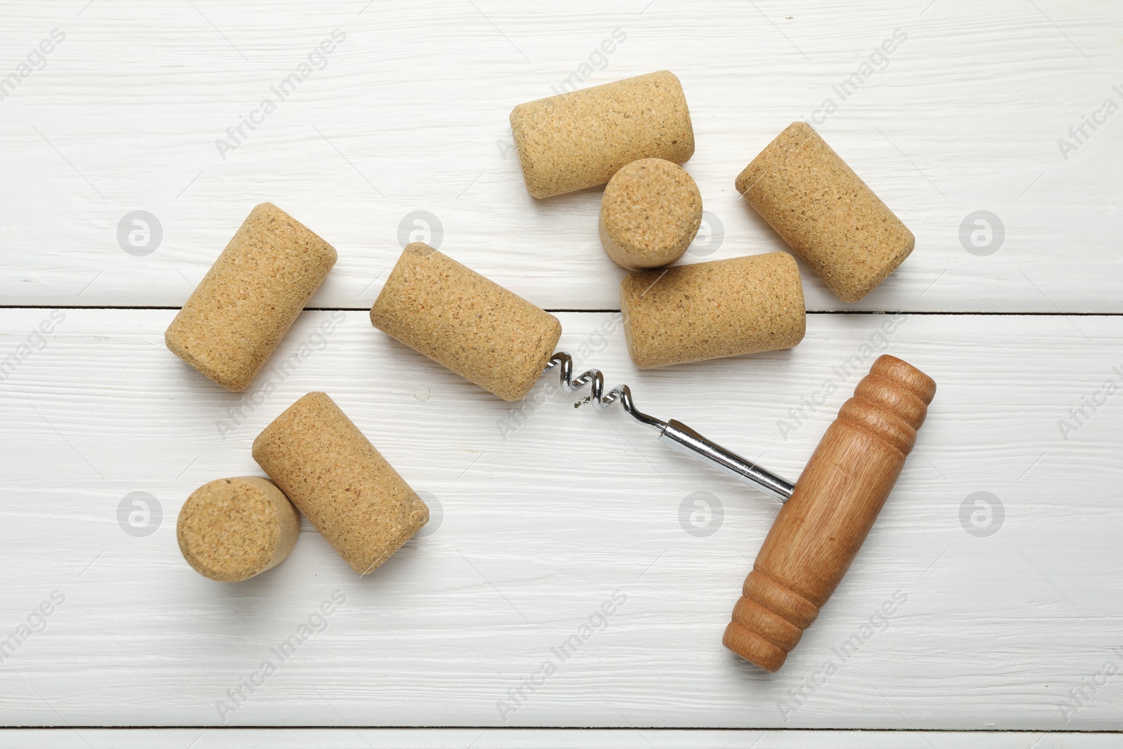 Photo of Corkscrew and corks on white wooden table, flat lay