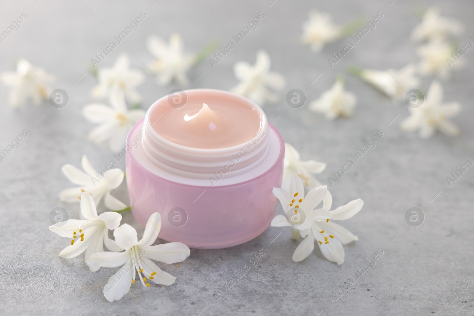 Photo of Cream in jar and jasmine flowers on grey table, closeup