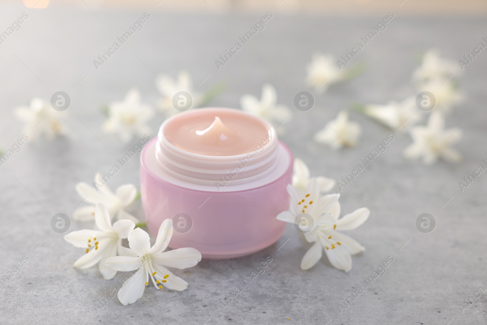 Photo of Cream in jar and jasmine flowers on grey table, closeup